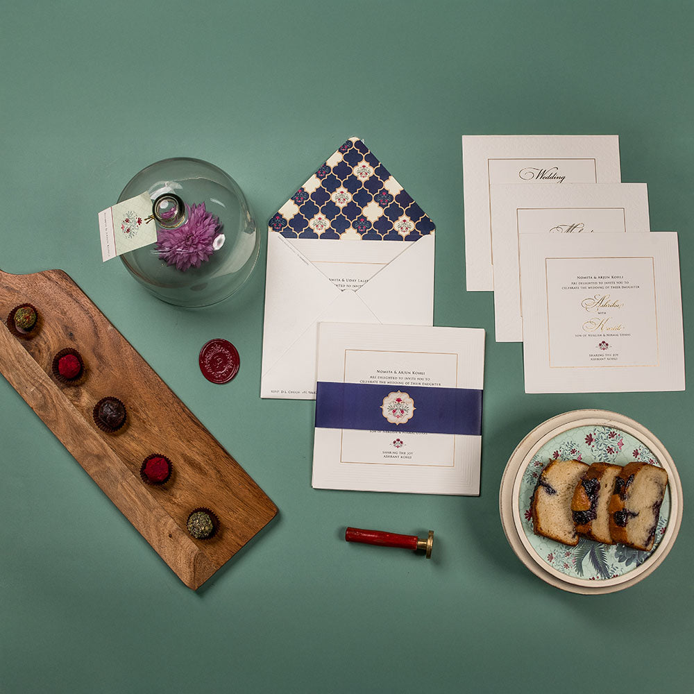 Elegant navy and cream wedding invite with blue floral motifs and desserts in frame.