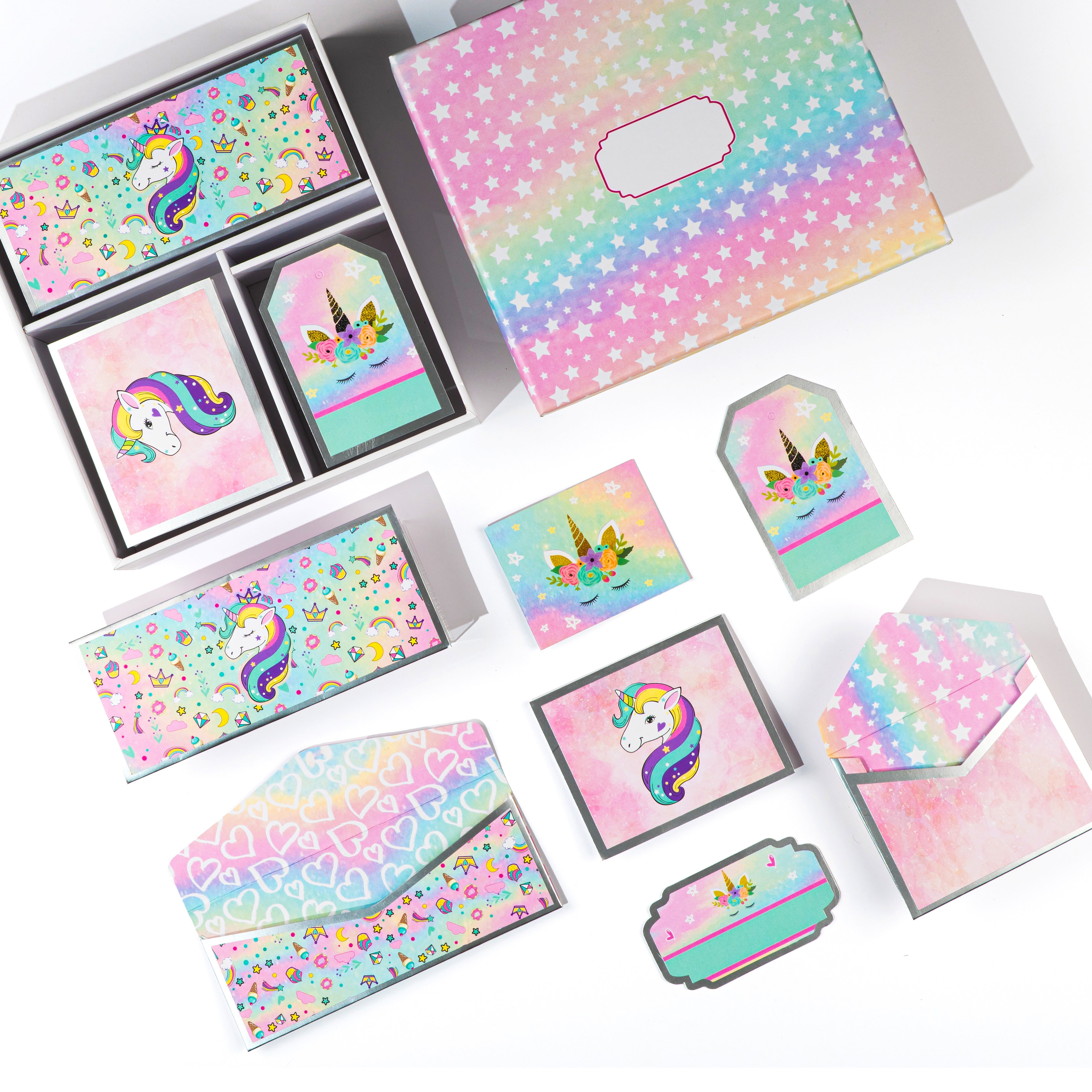 Whimsical unicorn-themed stationery gift set with pastel rainbow envelopes, folded cards, gift tags, and sticker tags arranged in a box.
