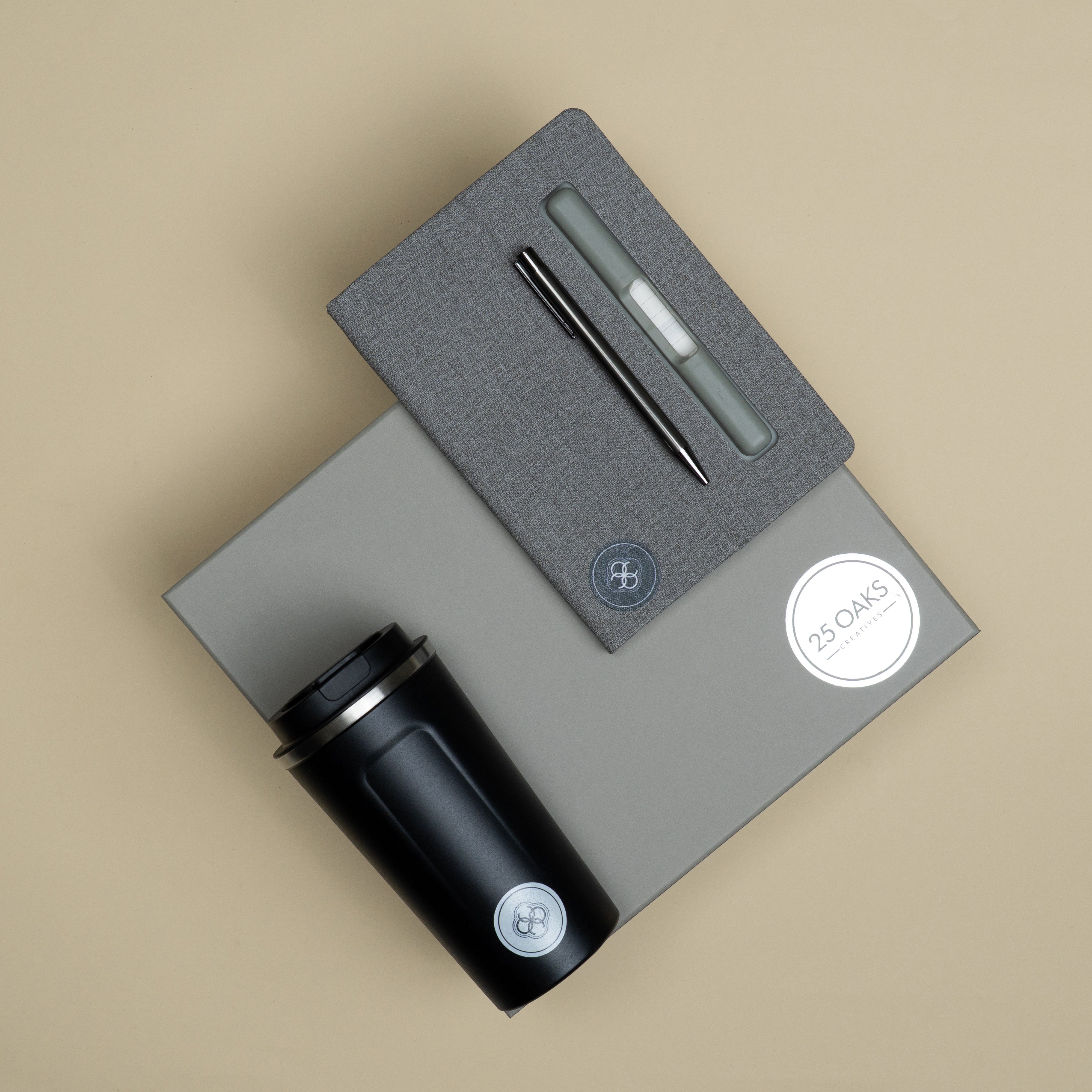 corporate gift set featuring a grey diary with pen holder and phone stand, metallic pen, black travel tumbler and branded cardboard gift box with grass cavity.