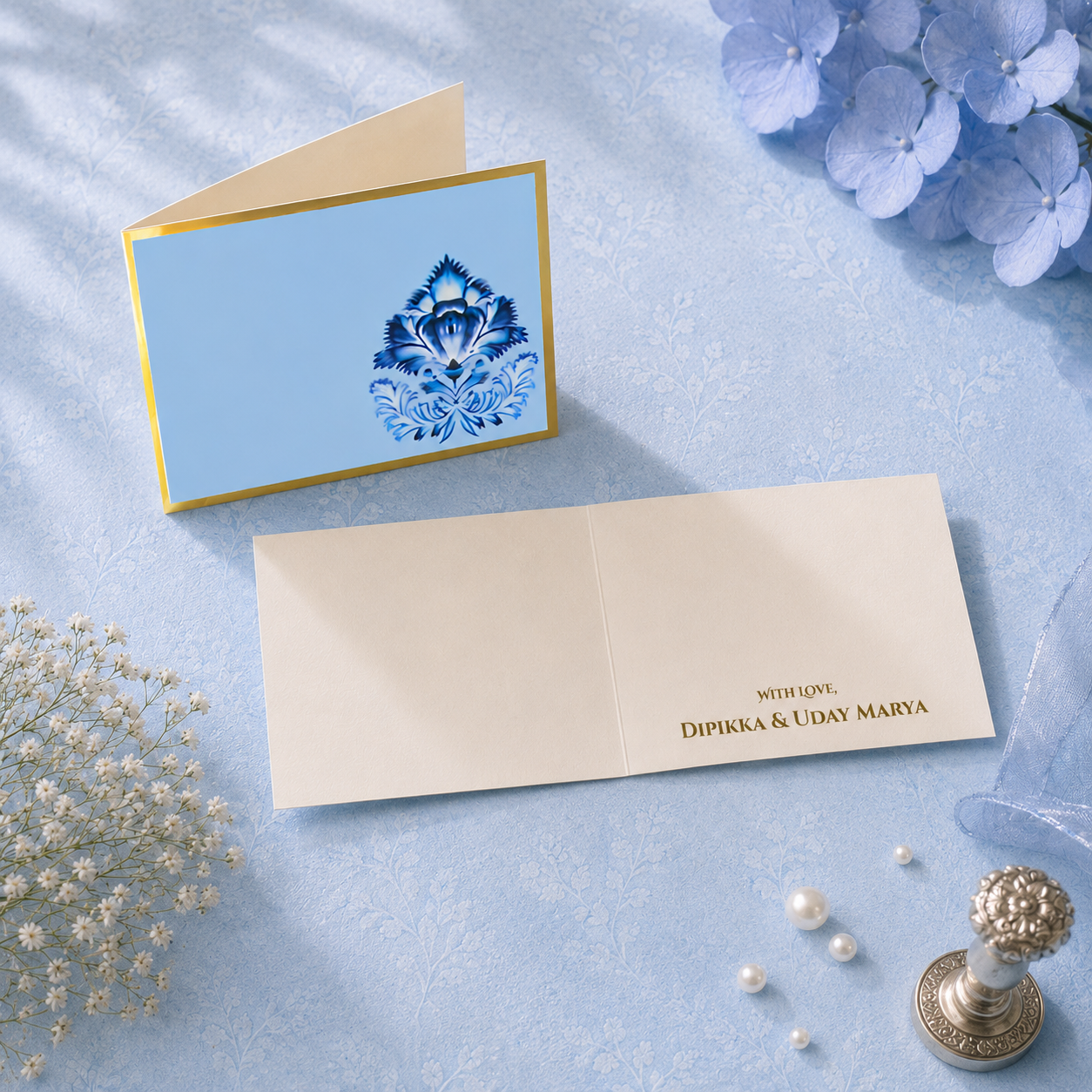 Luxury personalised folded card in a blue batik-inspired design featuring gold foil accents, pearl props, and refined floral styling.
