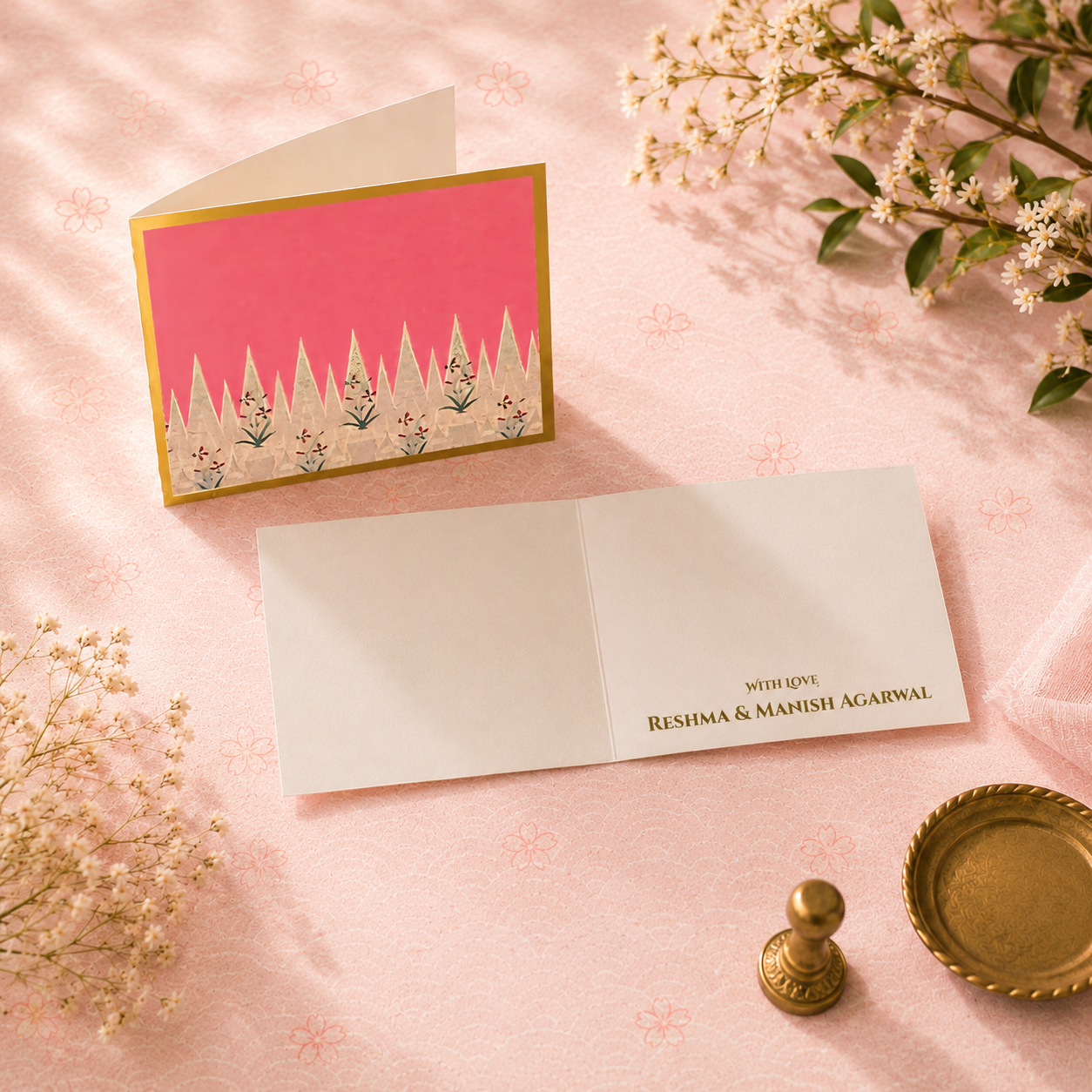 Luxury pink folded card with artistic cypress-inspired design, gold border detailing, and elegant ivory interiors styled with floral props.