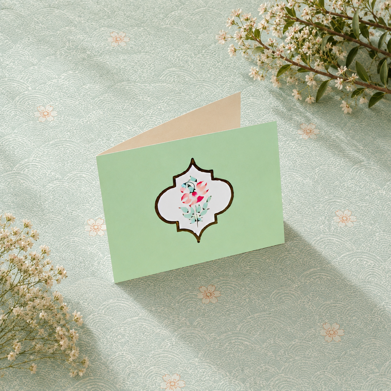 Luxury mint green folded card with delicate lotus-inspired motif and elegant ivory interiors styled with floral accents and gold props.