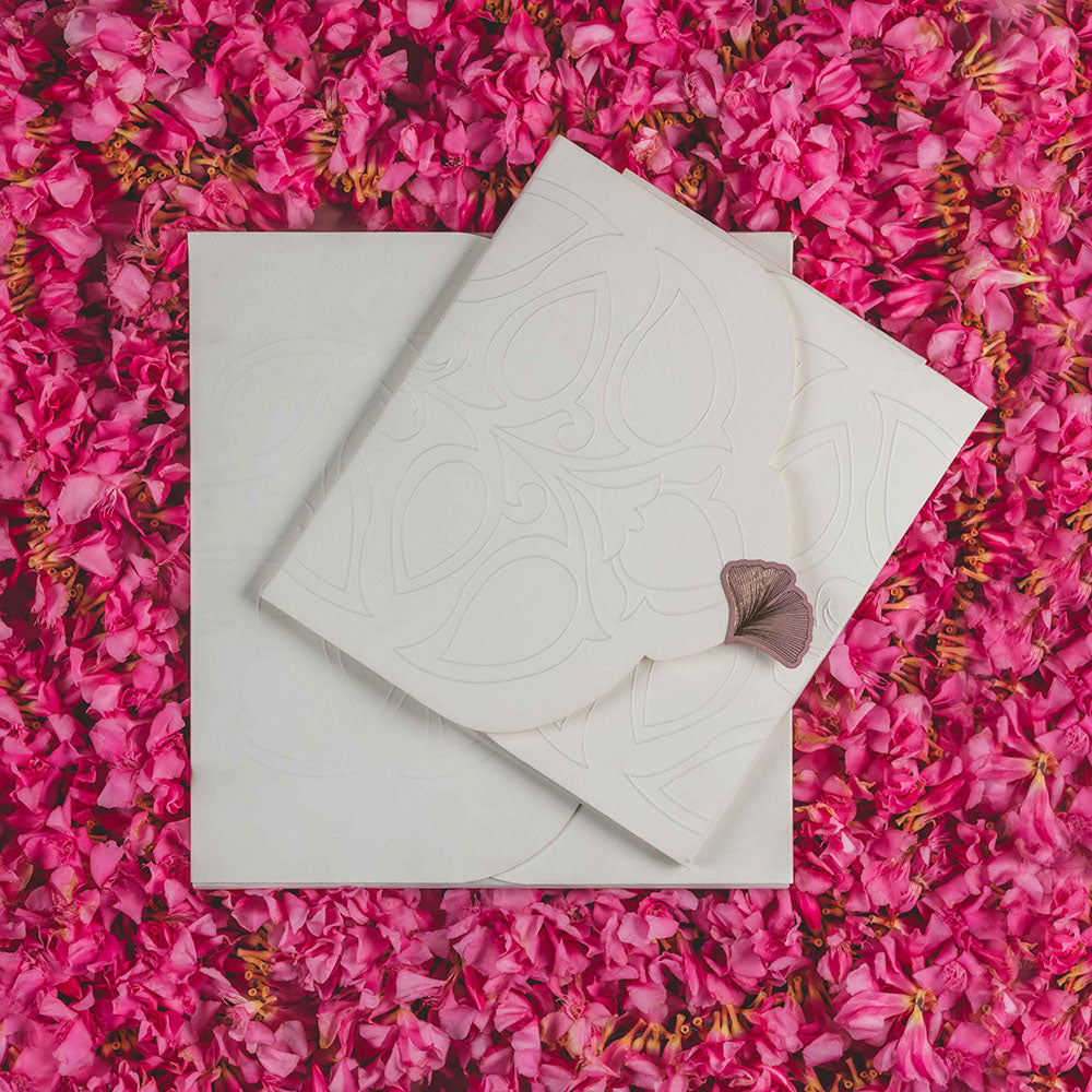 Minimalist ivory wedding invite with embossed paisley design and ginkgo leaf clasp.
