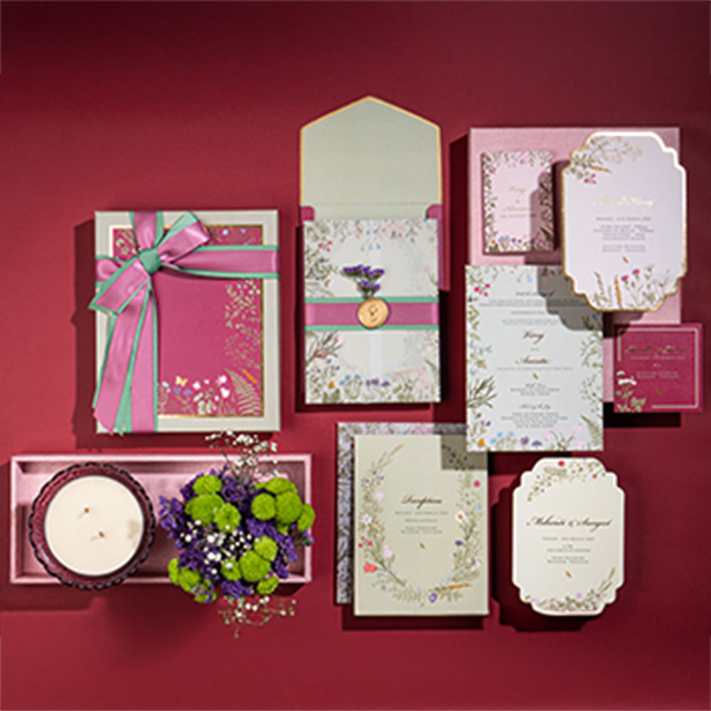 Botanical-themed wedding invite set in sage and fuchsia with florals, wax seals, and vintage bowl candle.