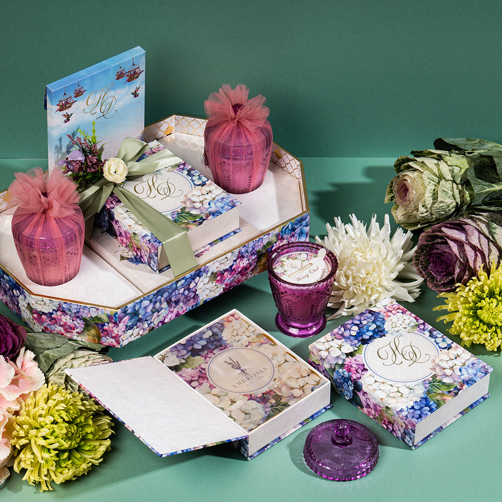 Floral gift hamper with violet candles, Ludhiana sweets, and treats in a hydrangea-themed keepsake tray.