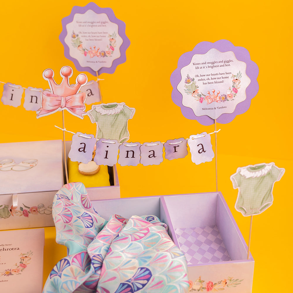 Pastel baby announcement gift tray with scarf, pocket square, cookies, and tea cakes.
