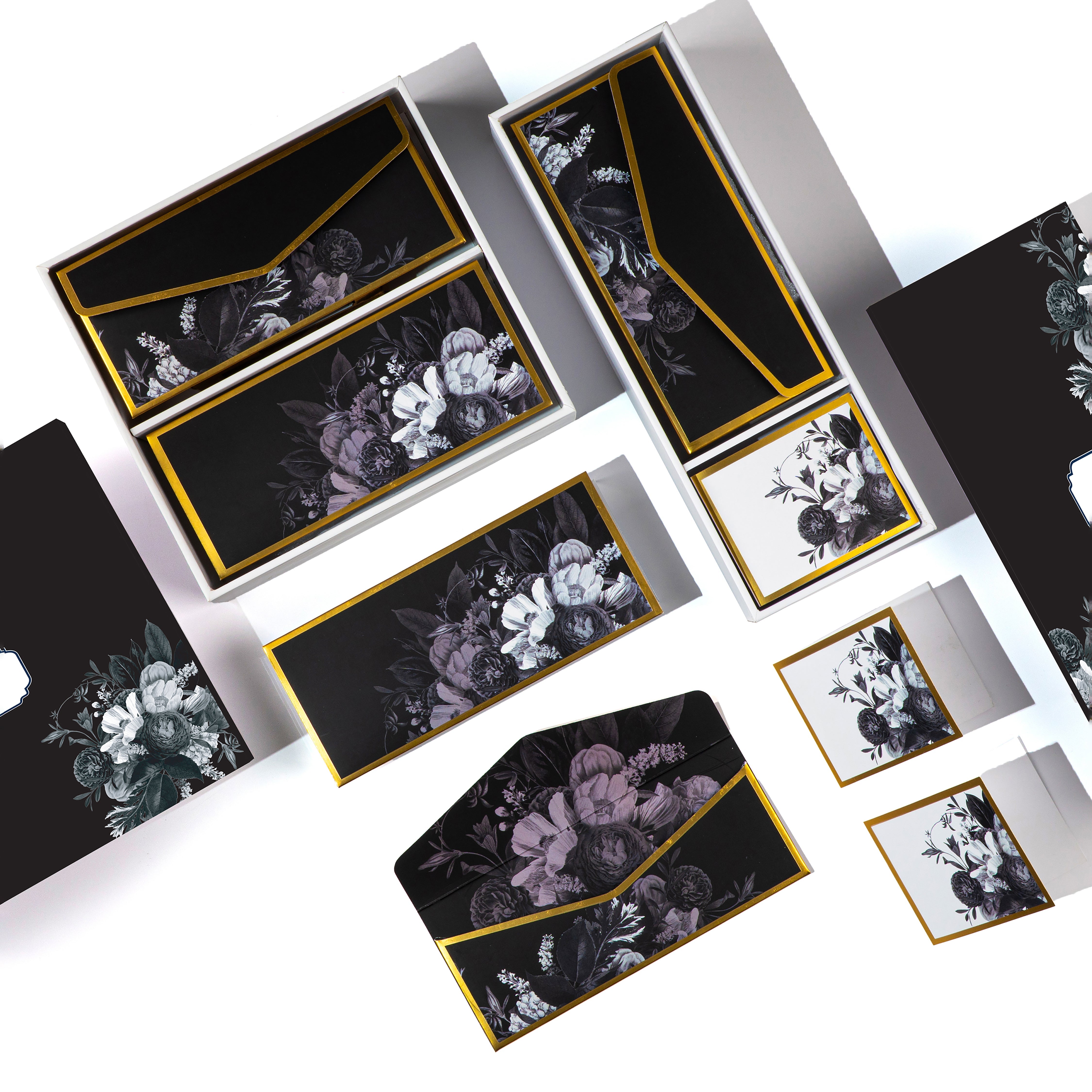 Luxury black floral stationery set with envelopes, cards, and boxes featuring gold trim and elegant botanical designs.