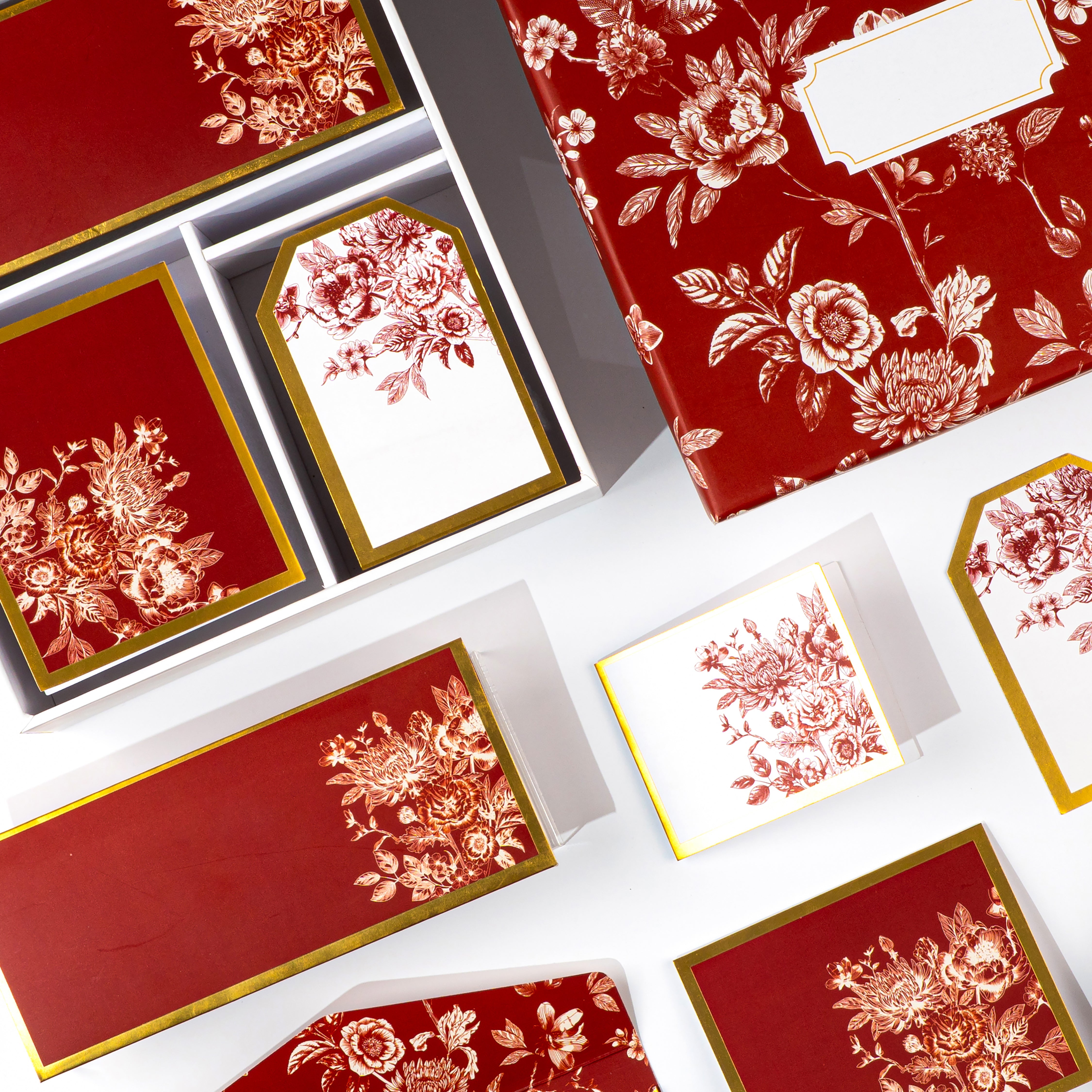 Elegant red and gold boxed stationery with rose‑patterned cards, envelopes, and tags.
