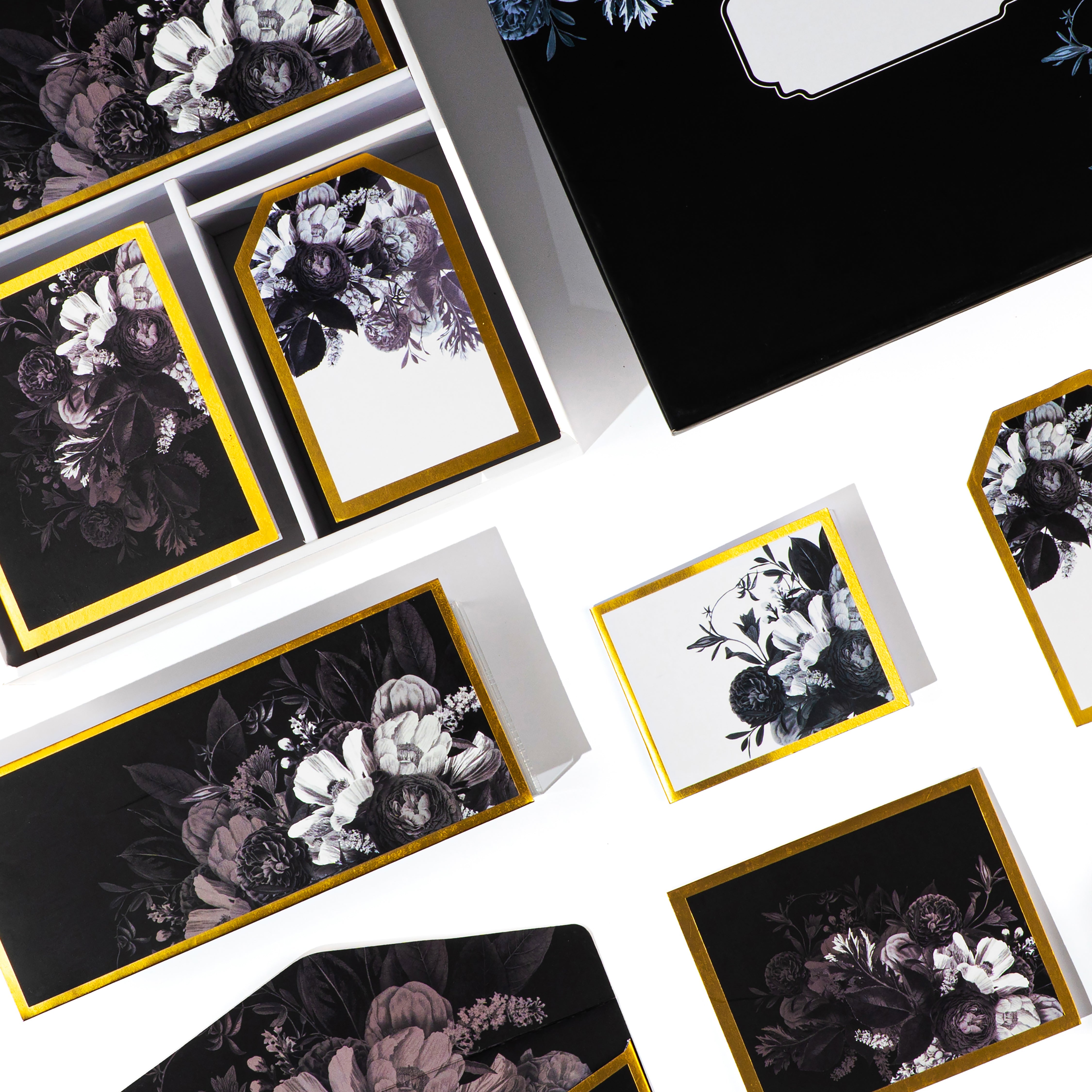 Luxury black floral stationery set with envelopes, cards, and boxes featuring gold trim and elegant botanical designs.