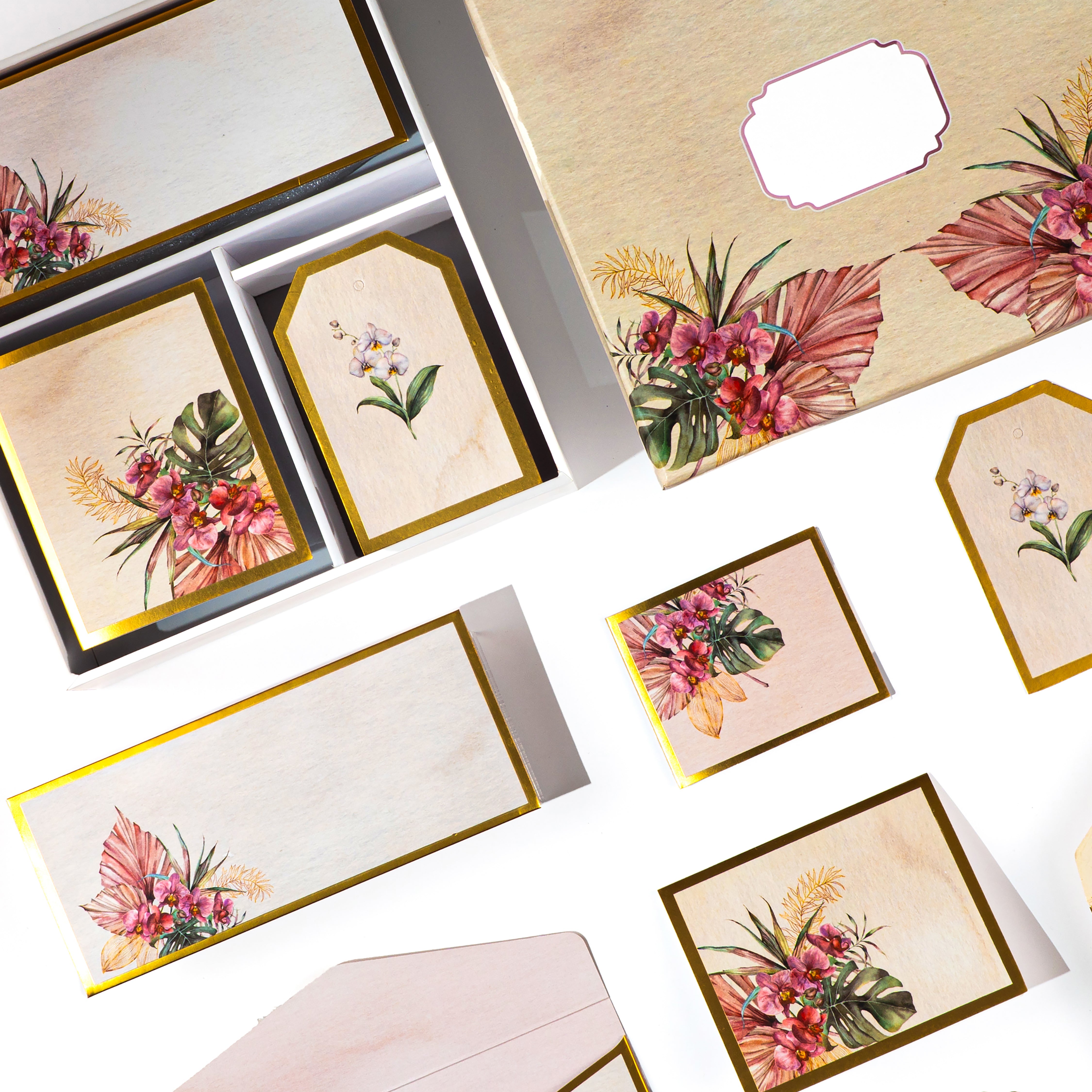 Tropical floral stationery set with gold accents, featuring tags, cards, and envelopes in a wooden-look box.