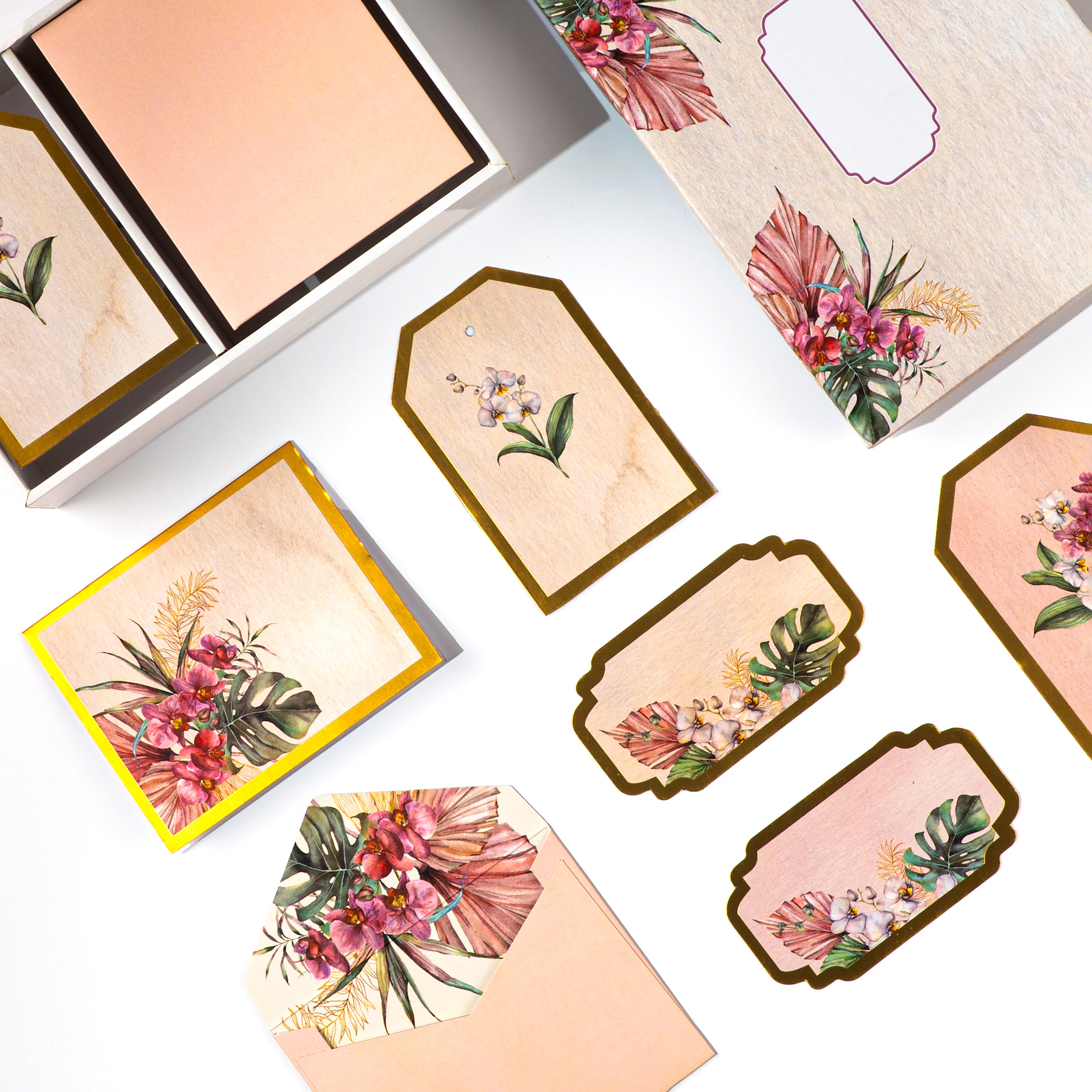 Tropical floral stationery set with gold accents, featuring tags, cards, and envelopes in a wooden-look box.