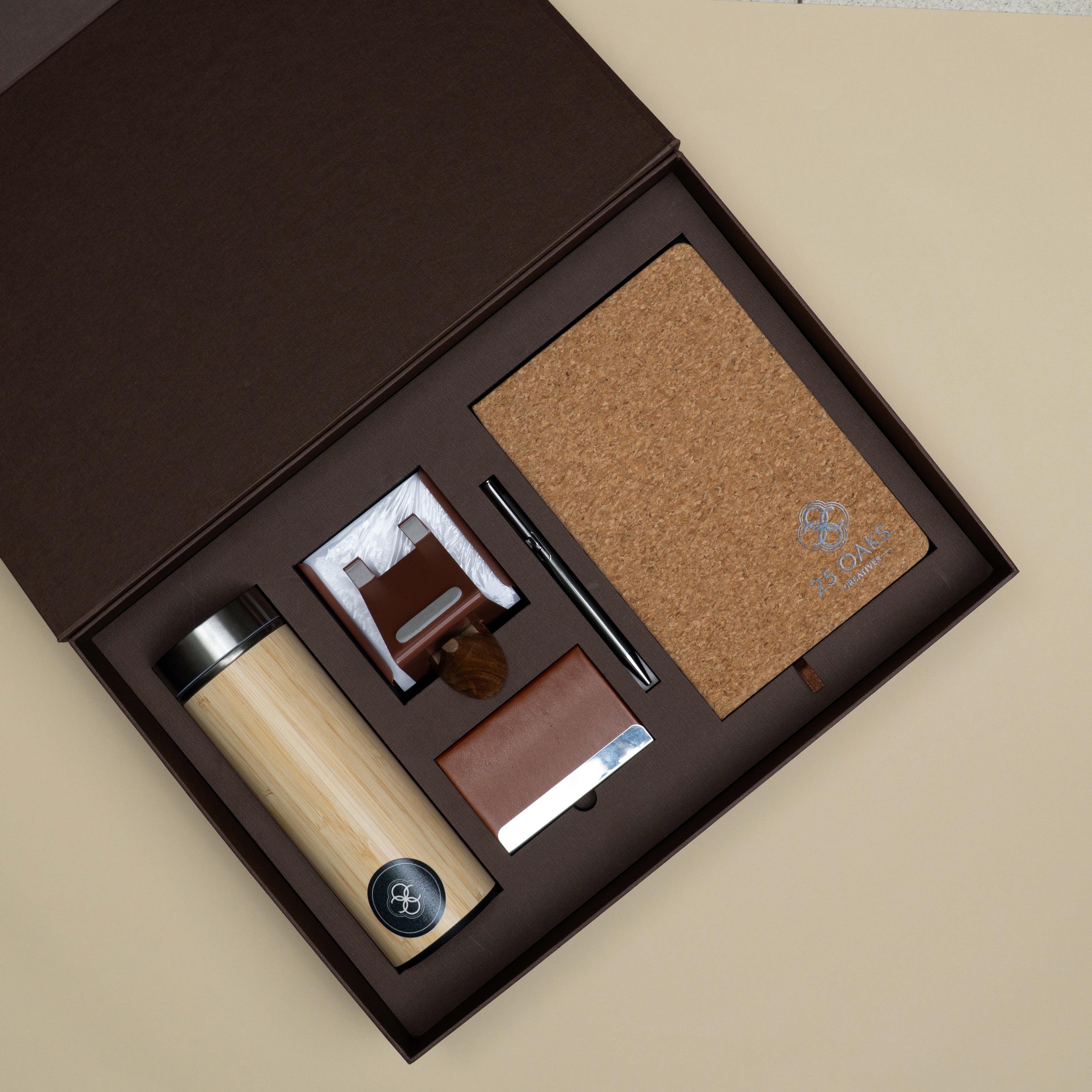 Premium corporate gift set with diary, metallic pen, bamboo bottle, card holder, phone stand, writing pad and specs holder in a branded cardboard box.