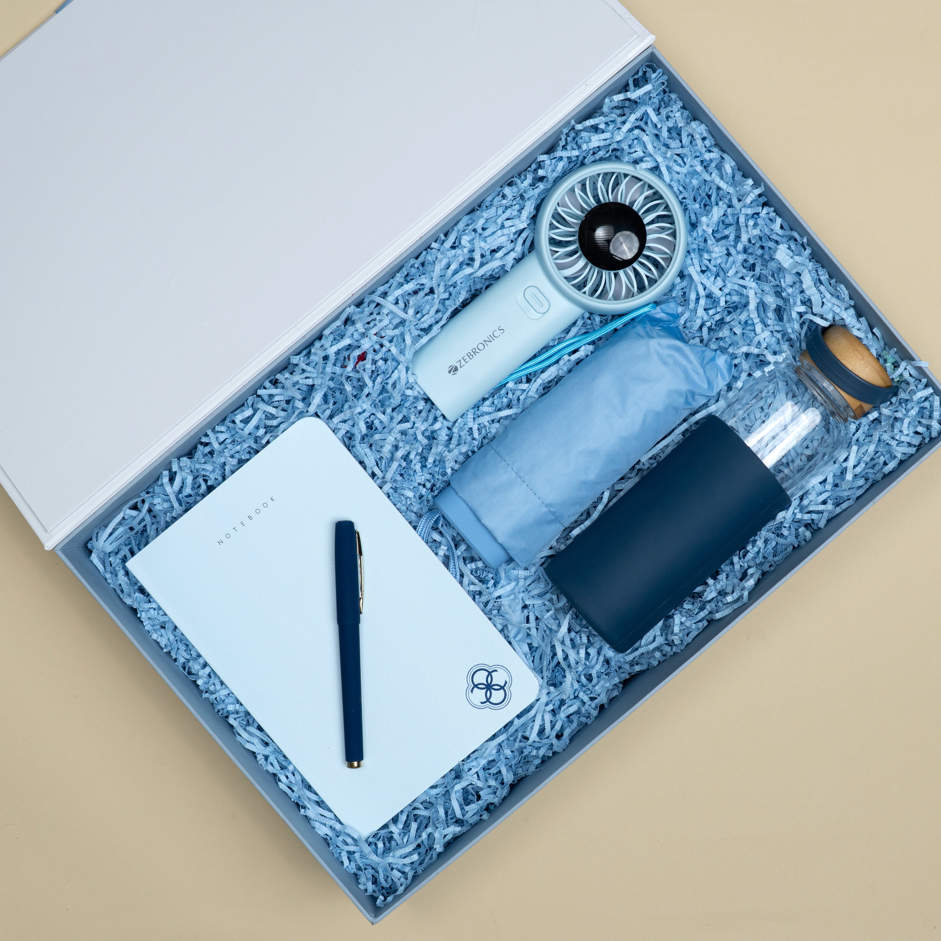 The Breeze sky blue corporate gift set featuring a Classic A5 notebook, mini pocket-friendly umbrella, portable hand fan, matte blue pen and glass jar bottle.