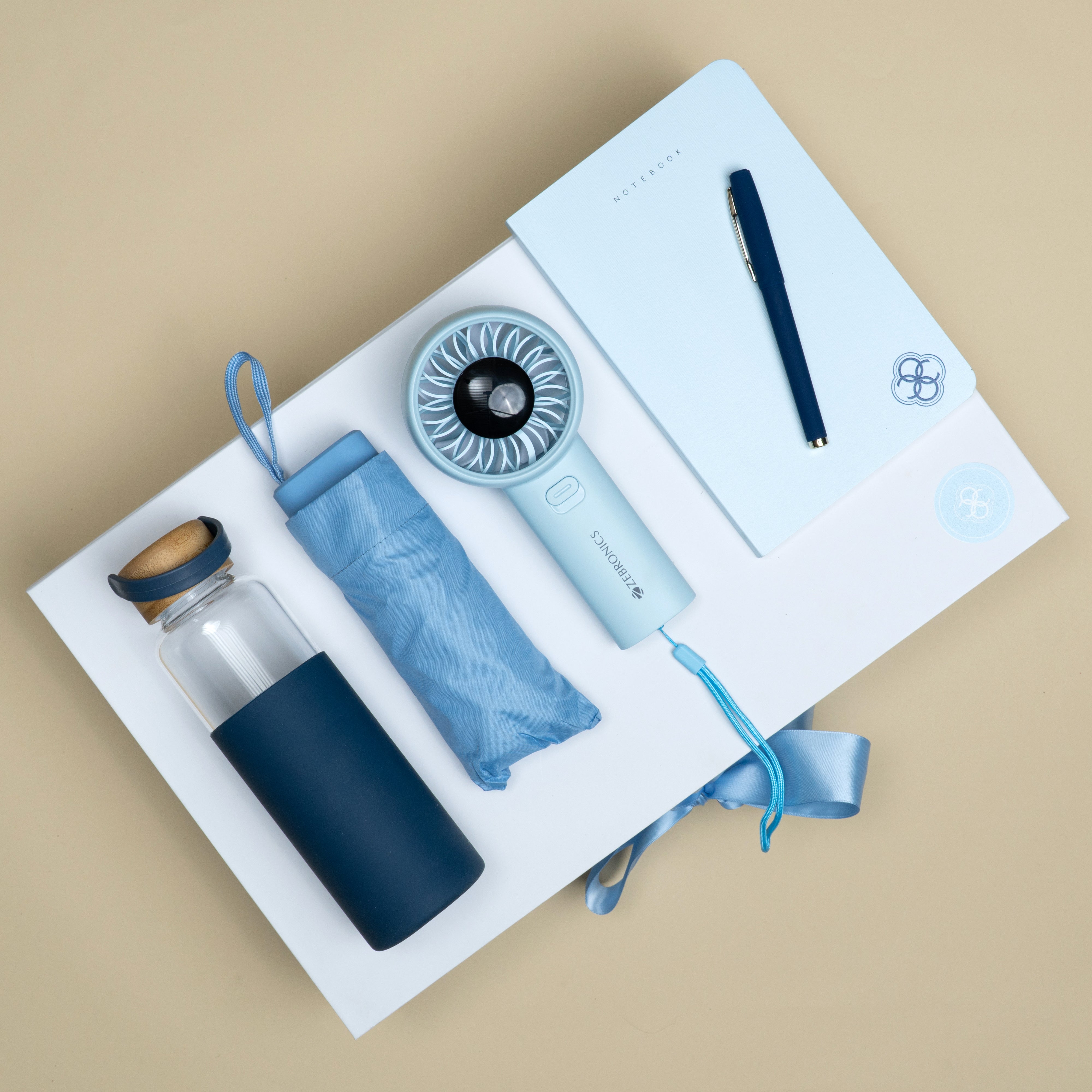 Sky blue corporate gift set with A5 notebook, mini umbrella, hand fan, blue pen and glass bottle.