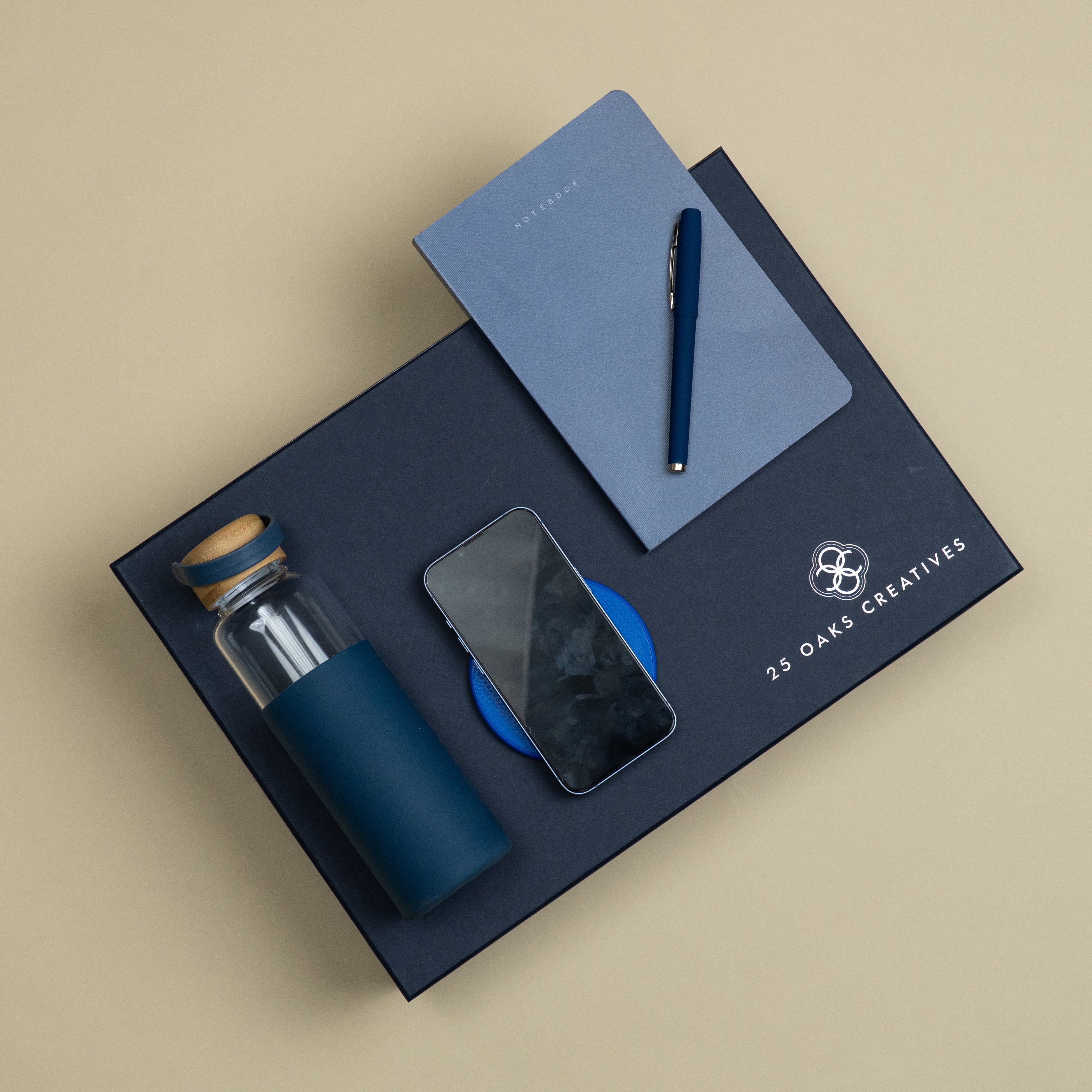 Plugged In blue corporate gift set featuring a glass bottle with silicone grip, wireless charger, matte blue pen and Classic A5 soft-cover notebook.